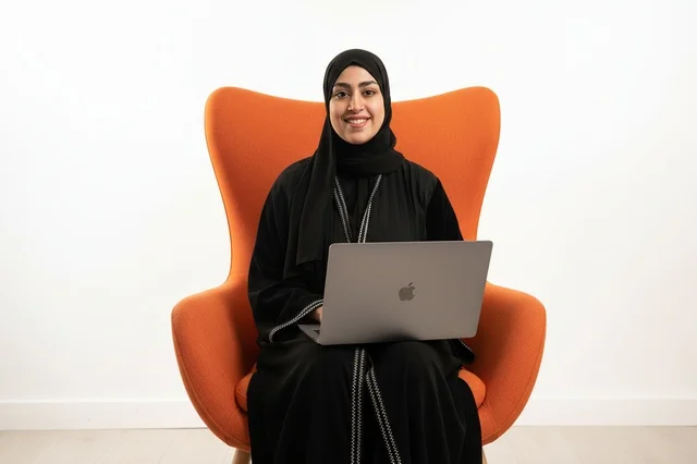 امرأة إماراتية مع لابتوب على كرسي برتقالي امرأة إماراتية مع لابتوب على كرسي برتقالي