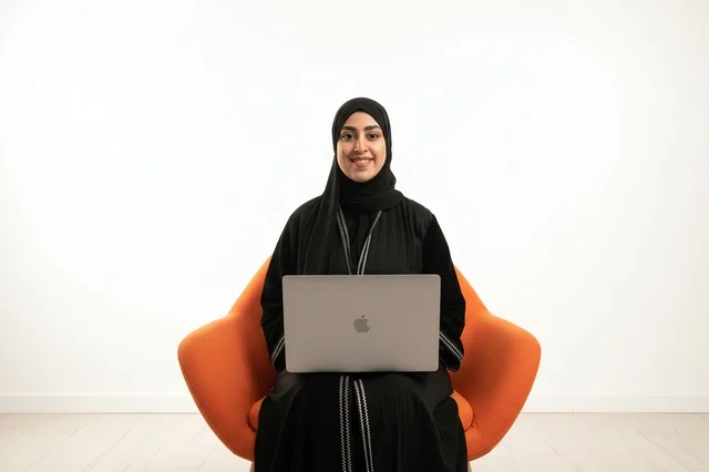 امرأة إماراتية مع كمبيوتر محمول على كرسي برتقالي