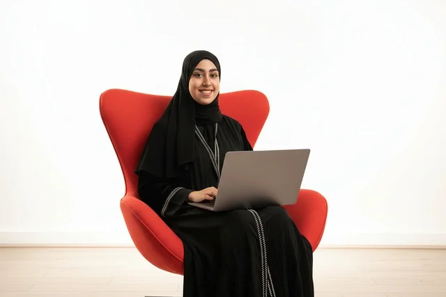 امرأة إماراتية بالعباءة تستخدم المحمول على كرسي أحمر