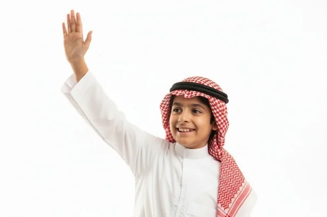 طفل سعودي بالثوب التقليدي يلوح بيده على خلفية بيضاء