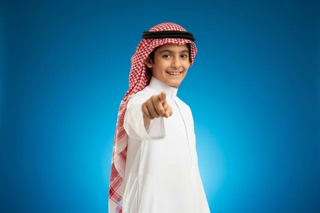 طفل سعودي بالثوب التقليدي يشير للكاميرا