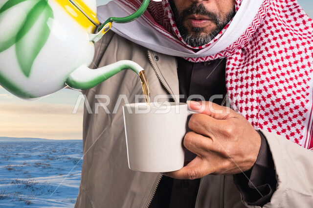 رجل عربي خليجي سعودي  يحمل بيده ابريق الشاي وكوب، رجل يسكب مشروب الشاي الساخن في الكوب، مشروبات دافئة، ابريق شاي، رحلة ترفيهية ، اجواء شتوية 