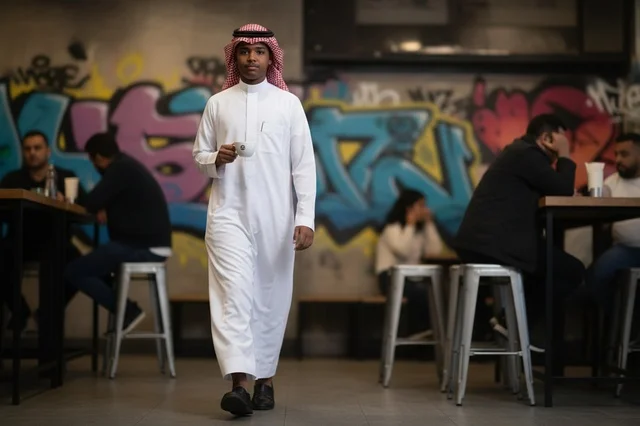 شاب سعودي بالثوب التقليدي داخل مقهى عصري
