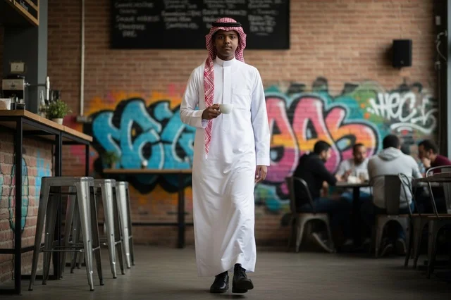 شاب سعودي بالثوب التقليدي داخل مقهى عصري