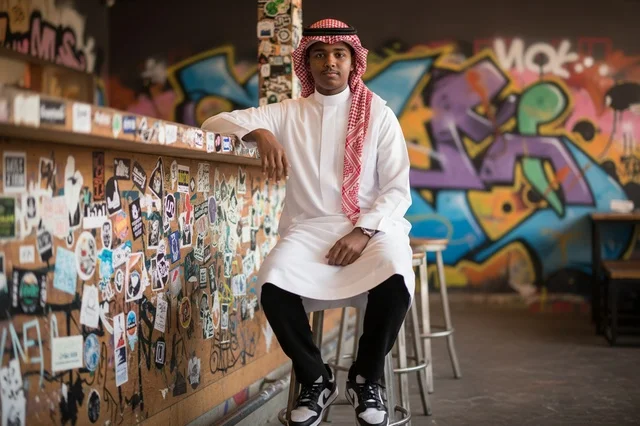 شاب سعودي بالثوب والشماغ أمام جدار غرافيتي
