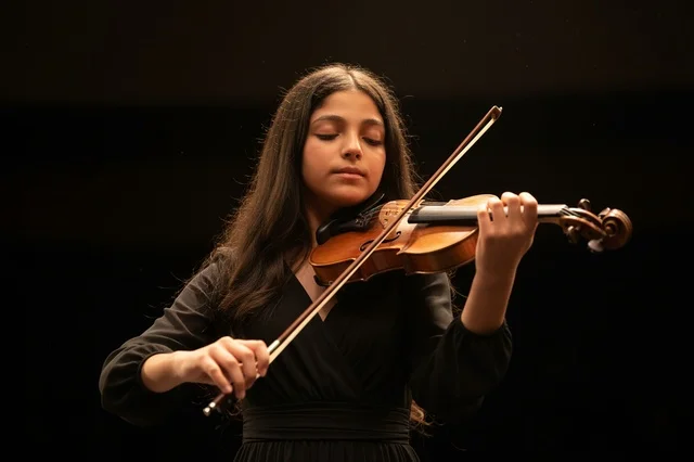 Saudi Girl Playing Violin on Dark Stage Background