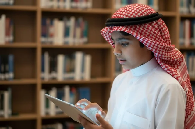 Saudi Boy in Traditional Thobe Using Tablet in Library
