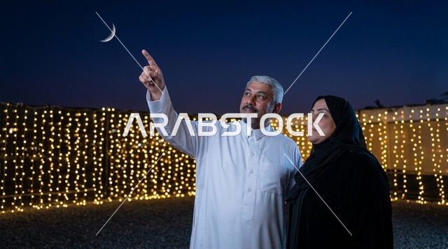 رجل وامرأة سعوديان يراقبان هلال القمر في السماء