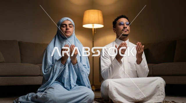 رجل وامرأة من السعودية يؤديان الدعاء في إضاءة دافئة