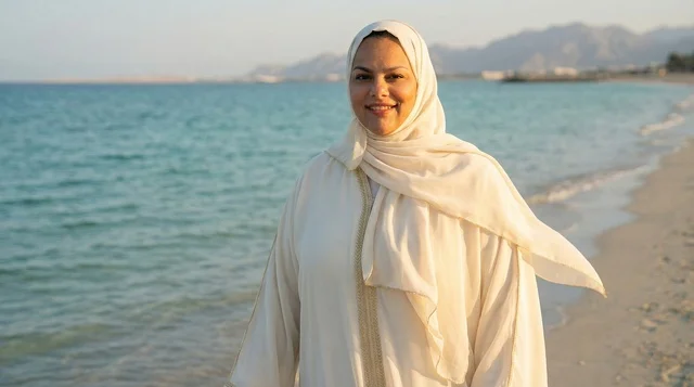 امرأة سعودية بعباية بيضاء على الشاطئ وقت الغروب