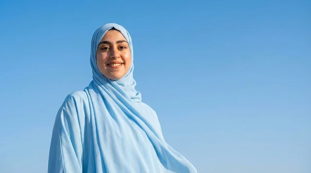 امرأة سعودية مبتسمة بالحجاب الأزرق والسماء الصافية