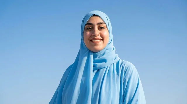 امرأة سعودية مبتسمة ترتدي حجاب أزرق تحت السماء