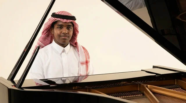 شاب سعودي بالزي التقليدي يجلس أمام بيانو أسود كبير
