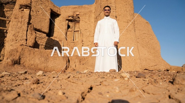رجل سعودي بالثوب التقليدي أمام أطلال طينية قديمة