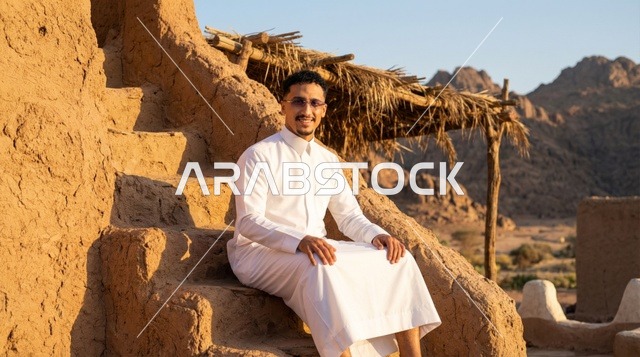 رجل سعودي بالثوب الأبيض عند مبنى طيني تراثي قديم