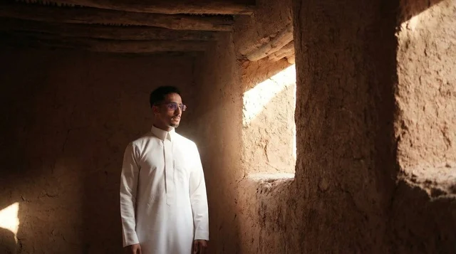 A Saudi man in traditional attire at a desert heritage site.