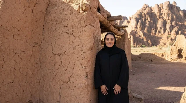 امرأة سعودية بالعباءة أمام مبنى طيني قديم في الصحراء
