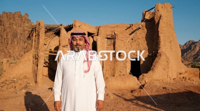 رجل سعودي يقف أمام منزل طيني قديم