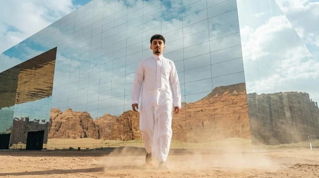 شاب سعودي يمشي أمام مبنى مرايا في العلا