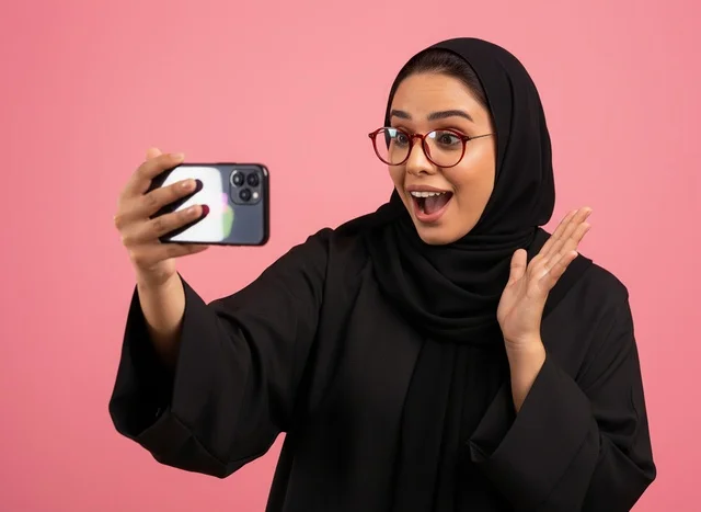 Surprised Saudi Woman with Smartphone on Pink Background