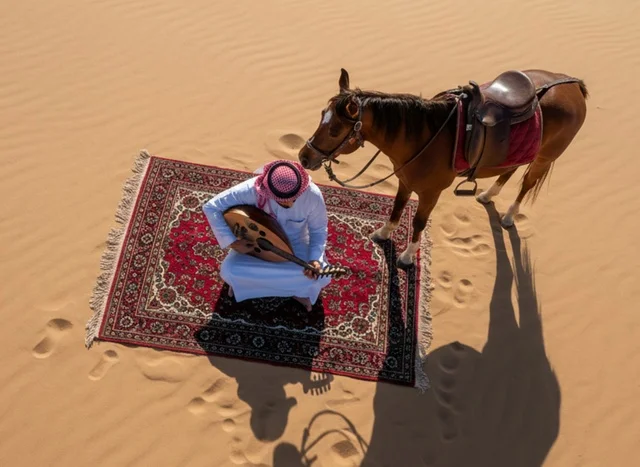 رجل سعودي يعزف العود مع خيل عربي في الصحراء
