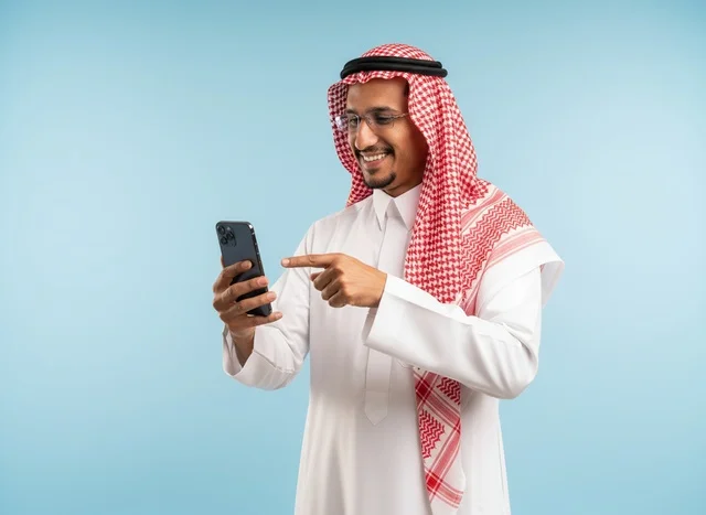 رجل سعودي بالثوب يشير إلى شاشة الهاتف الذكي
