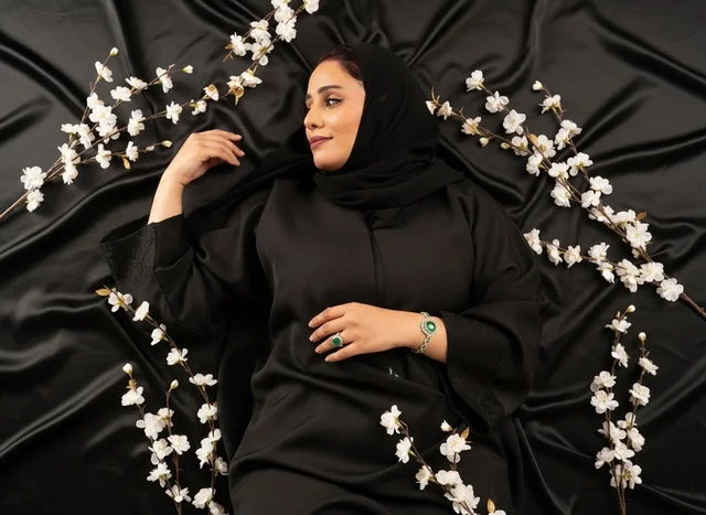 امرأة سعودية بالعباءة السوداء مع زهور بيضاء على ساتان