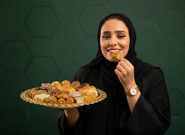 امرأة سعودية بالعباءة تتناول الحلويات الشرقية التقليدية