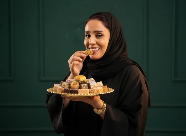 امرأة سعودية بالعباءة تتناول الحلويات العربية التقليدية