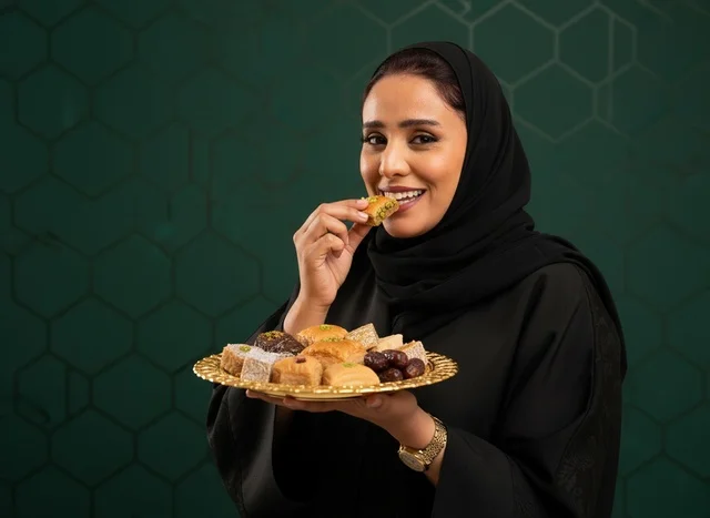 امرأة سعودية مع حلويات عربية تقليدية وبقلاوة