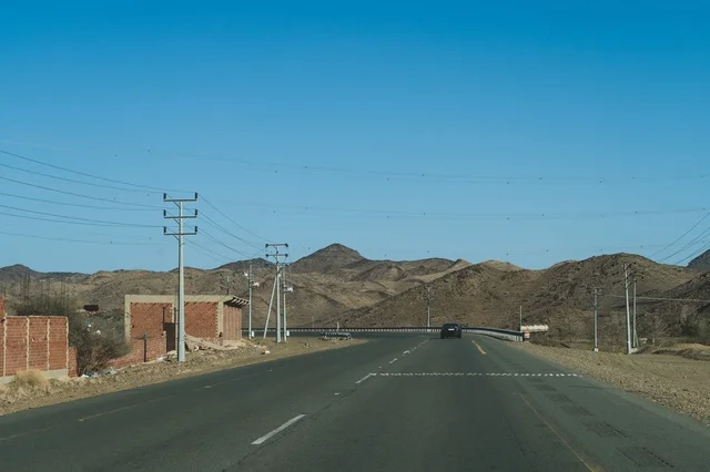 Asphalt Highway Through Desert Mountains Under Blue Sky