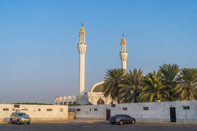 مسجد أبيض بمآذن شاهقة وأشجار نخيل تحت سماء صافية