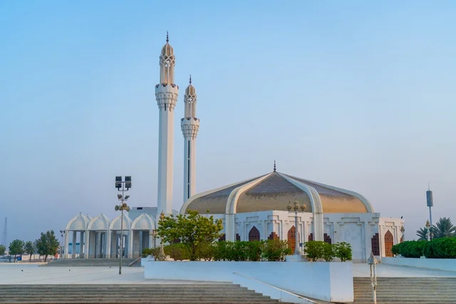 Architectural design of a modern white mosque with a distinctive golden dome.