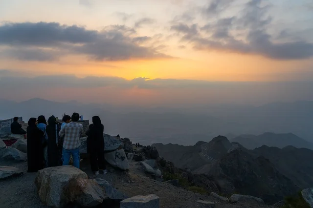 سياح على قمة جبل يشاهدون غروب الشمس