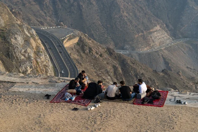 رجال سعوديون في نزهة فوق جبل يطل على طريق سريع متعرج