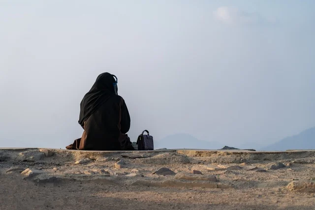 امرأة عربية بالعباءة تجلس على حافة جبلية