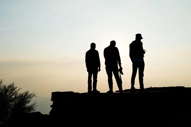 Silhouette of Men Standing on a Mountain Cliff at Sunrise