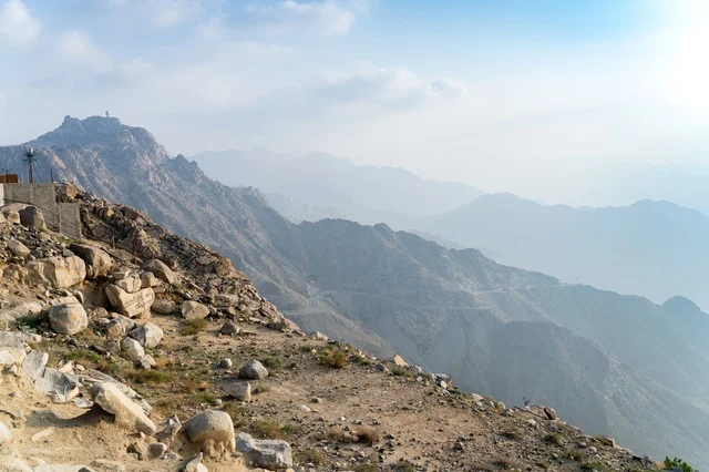 قمة جبلية صخرية مع سلسلة جبال ضبابية في وضح النهار
