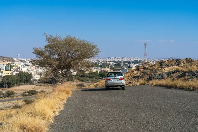 Silver Car on Mountain Road Heading to City Under Blue Sky