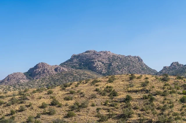 A landscape of barren mountains with a road and modern domes during the day.