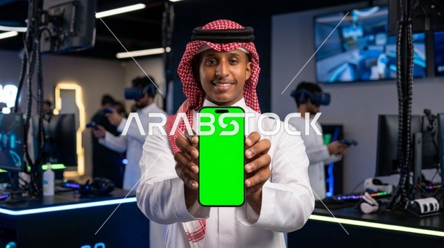 رجل سعودي يحمل هاتف بشاشة خضراء في صالة ألعاب