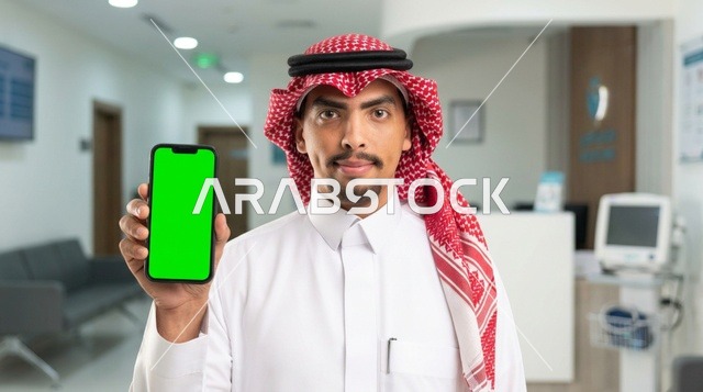 رجل سعودي يحمل هاتف ذكي بشاشة خضراء في العيادة الطبية