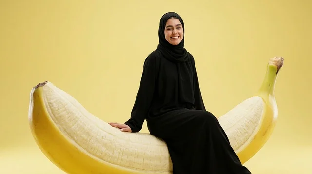 An Arab woman in a black abaya sits on a giant banana sculpture.