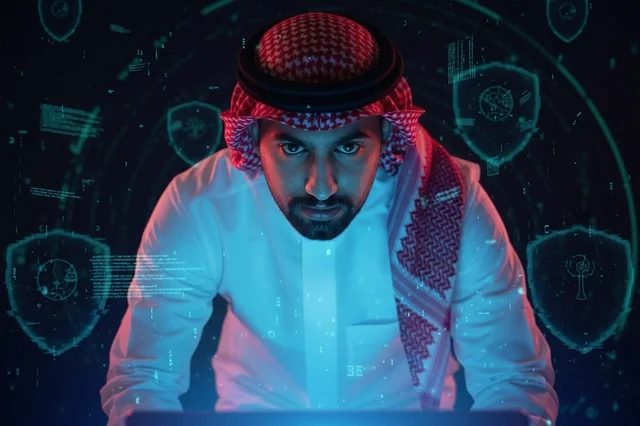 مبرمج سعودي وخبير أمن سيبراني أمام شاشات رقمية