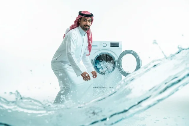 رجل سعودي بجانب غسالة ملابس مع رذاذ ماء متطاير