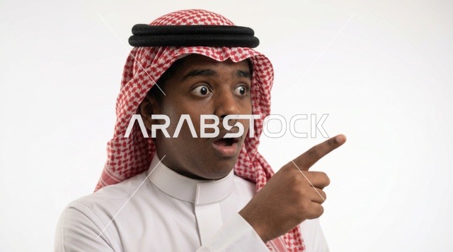 رجل سعودي متفاجئ يشير بإصبعه أمام خلفية بيضاء استوديو