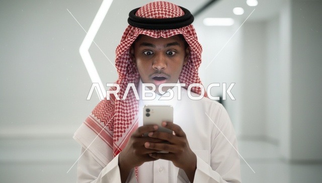 رجل سعودي مصدوم ينظر إلى شاشة هاتفه الذكي المضيئة