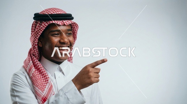 شاب سعودي يبتسم ويشير بإصبعه على خلفية استوديو بيضاء