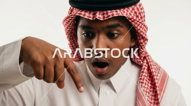 رجل سعودي متفاجئ ومصدوم يشير للأسفل على خلفية بيضاء