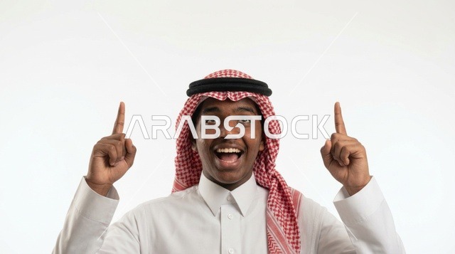 شاب سعودي مبتسم يشير بإصبعه للأعلى خلفية بيضاء